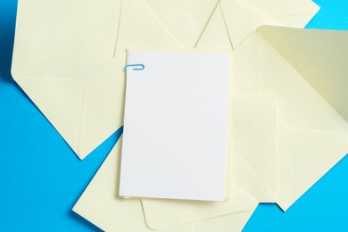 Photo of Blank invitation card and envelopes on light blue background, flat lay. Space for design