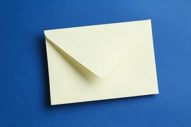 Photo of Beautiful invitation envelope on blue background, top view
