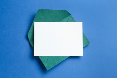 Photo of Blank invitation card and envelope on blue background, top view. Space for design