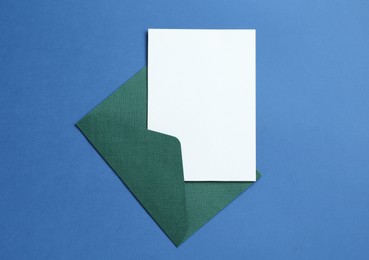 Photo of Blank invitation card and envelope on blue background, top view. Space for design