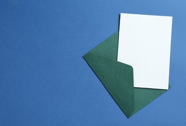 Photo of Blank invitation card and envelope on blue background, top view. Space for design