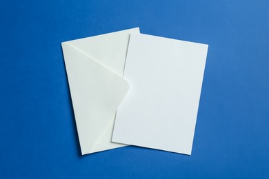 Photo of Blank invitation card and envelope on blue background, top view. Space for design