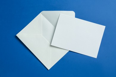 Photo of Blank invitation card and envelope on blue background, flat lay. Space for design