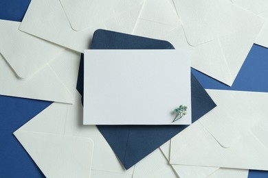 Photo of Blank invitation card and envelopes on blue background, flat lay. Space for design