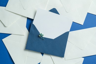 Photo of Blank invitation card and envelopes on blue background, flat lay. Space for design