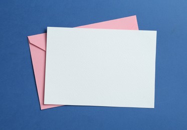 Photo of Blank invitation card and envelope on blue background, top view. Space for design