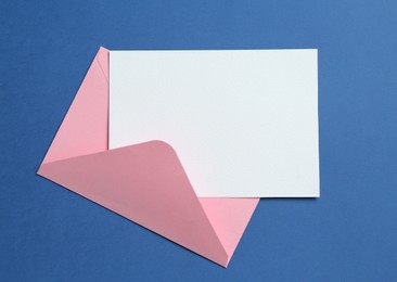 Photo of Blank invitation card and envelope on blue background, top view. Space for design