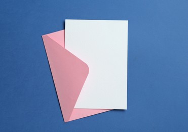 Photo of Blank invitation card and envelope on blue background, top view. Space for design