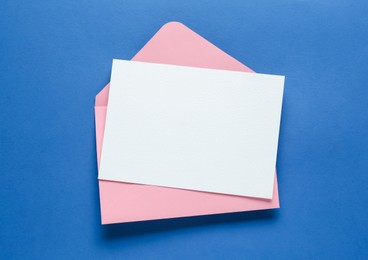Photo of Blank invitation card and envelope on blue background, top view. Space for design