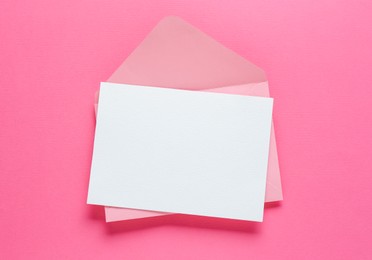 Photo of Blank invitation card and envelope on pink background, top view. Space for design
