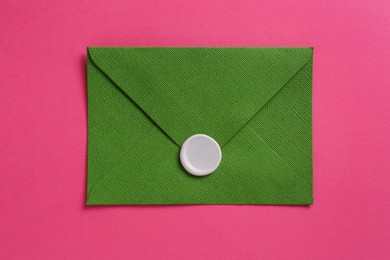 Photo of Beautiful invitation envelope with wax seal on pink background, top view