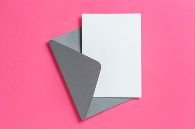 Photo of Blank invitation card and envelope on pink background, top view. Space for design