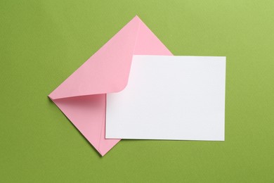 Photo of Blank invitation card and envelope on green background, top view. Space for design