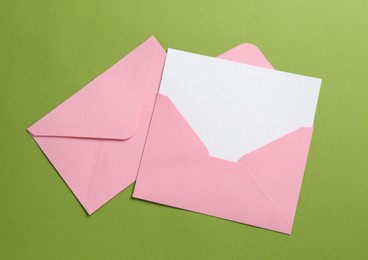 Photo of Blank invitation card and envelopes on green background, flat lay. Space for design