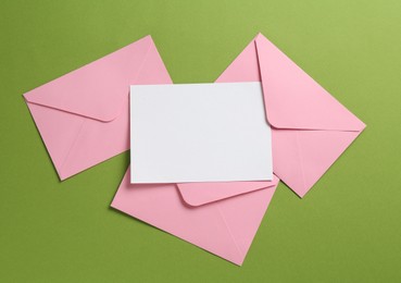 Photo of Blank invitation card and envelopes on green background, flat lay. Space for design