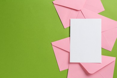 Photo of Blank invitation card and envelopes on green background, flat lay. Space for design