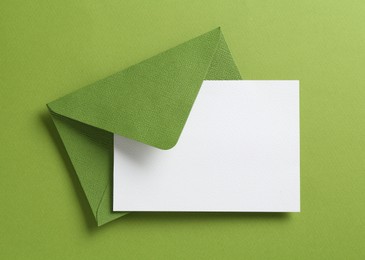 Photo of Blank invitation card and envelope on green background, top view. Space for design
