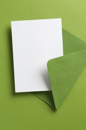 Photo of Blank invitation card and envelope on green background, top view. Space for design