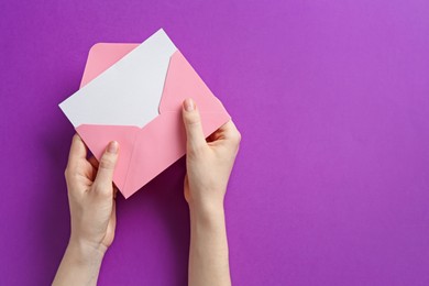 Photo of Woman holding envelope with blank invitation card on purple background, top view. Space for text