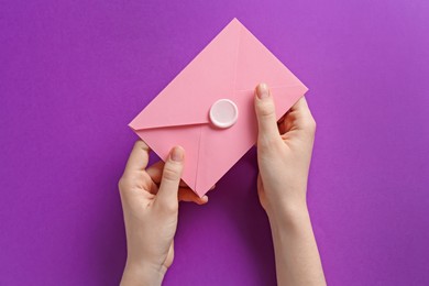 Photo of Woman holding beautiful invitation envelope with wax seal on purple background, top view