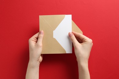Photo of Woman holding envelope with blank invitation card on red background, top view