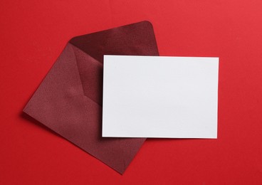 Photo of Blank invitation card and envelope on red background, top view. Space for design