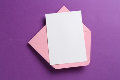 Photo of Blank invitation card and envelope on purple background, top view. Space for design