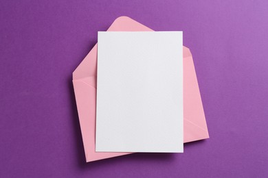 Photo of Blank invitation card and envelope on purple background, top view. Space for design