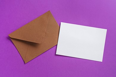 Photo of Blank invitation card and envelope on purple background, flat lay. Space for design