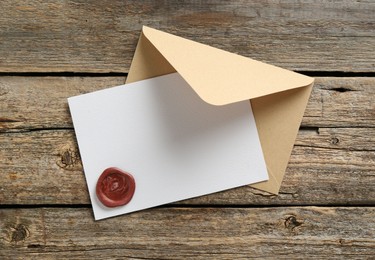 Photo of Blank invitation card with wax seal and envelope on wooden table, top view. Space for design