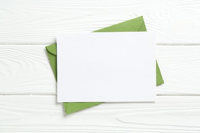 Photo of Blank invitation card and envelope on white wooden table, top view. Space for design