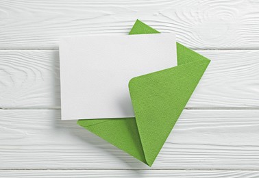 Photo of Blank invitation card and envelope on white wooden table, top view. Space for design