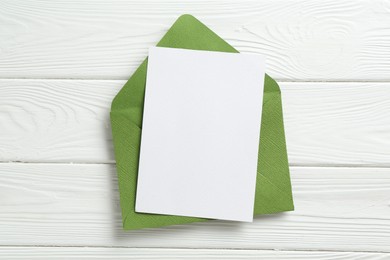 Photo of Blank invitation card and envelope on white wooden table, top view. Space for design