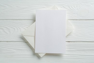 Photo of Blank invitation card and envelope on white wooden table, top view. Space for design