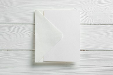 Photo of Blank invitation card and envelope on white wooden table, top view. Space for design