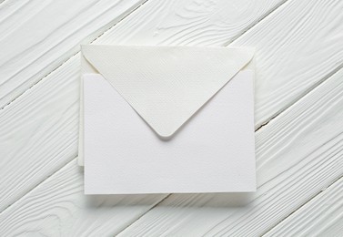 Photo of Blank invitation card and envelope on white wooden table, top view. Space for design