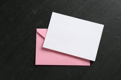Photo of Blank invitation card and envelope on black table, top view. Space for design