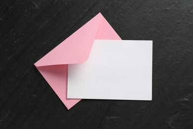 Photo of Blank invitation card and envelope on black table, top view. Space for design