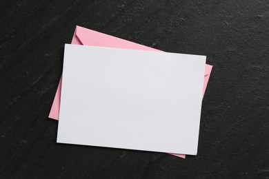Photo of Blank invitation card and envelope on black table, top view. Space for design