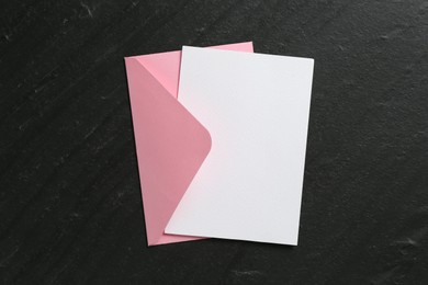 Photo of Blank invitation card and envelope on black table, top view. Space for design