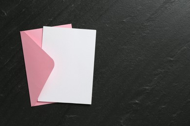 Photo of Blank invitation card and envelope on black table, top view. Space for design