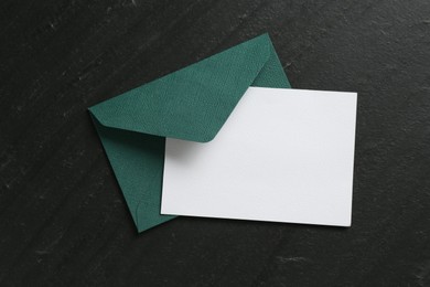 Photo of Blank invitation card and envelope on black table, top view. Space for design