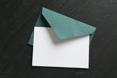 Photo of Blank invitation card and envelope on black table, top view. Space for design