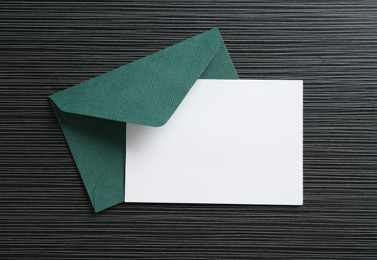 Photo of Blank invitation card and envelope on black textured table, top view. Space for design