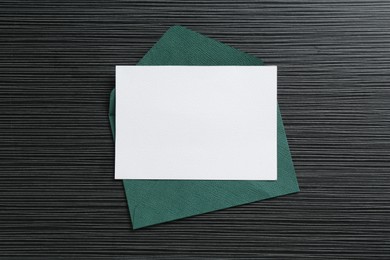 Photo of Blank invitation card and envelope on black textured table, top view. Space for design