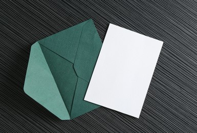 Photo of Blank invitation card and envelope on black textured table, top view. Space for design