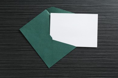 Photo of Blank invitation card and envelope on black textured table, top view. Space for design
