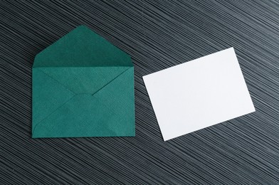 Photo of Blank invitation card and envelope on black textured table, flat lay. Space for design