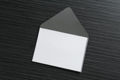 Photo of Blank invitation card and envelope on black textured table, top view. Space for design