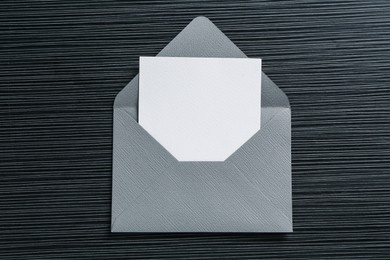 Photo of Blank invitation card and envelope on black textured table, top view. Space for design